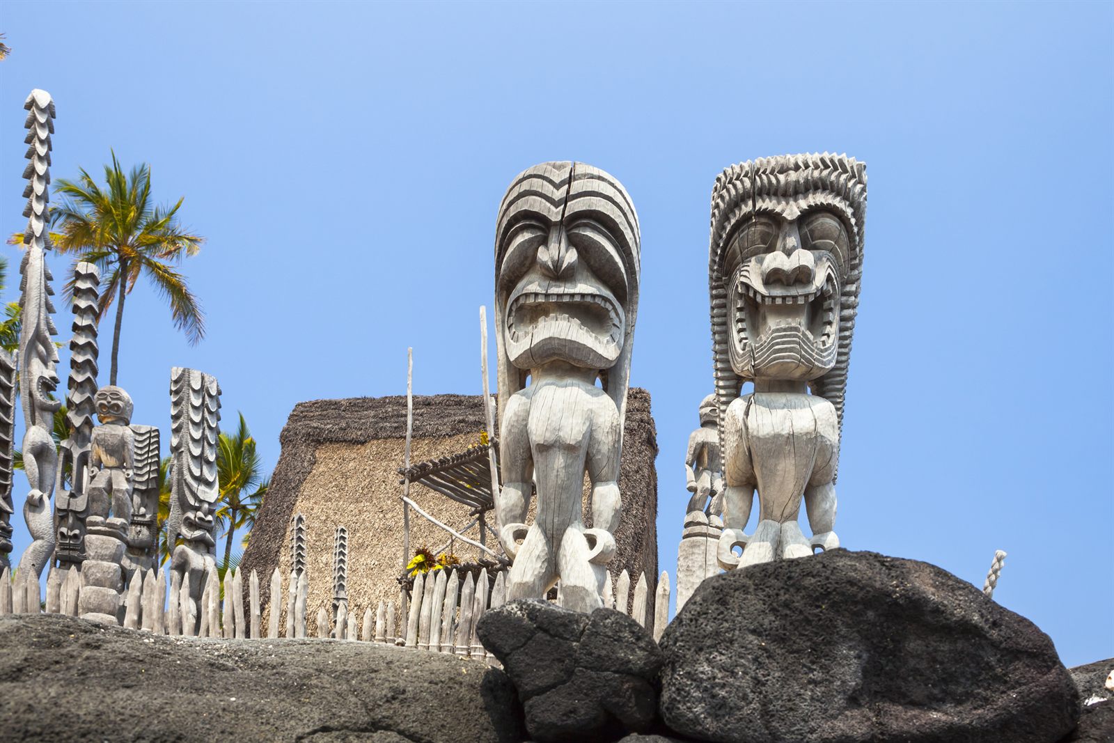 Carved wooden kii images and a thatched temple behind a lava rock wall at Puuhonua o Honaunau National Historical Park